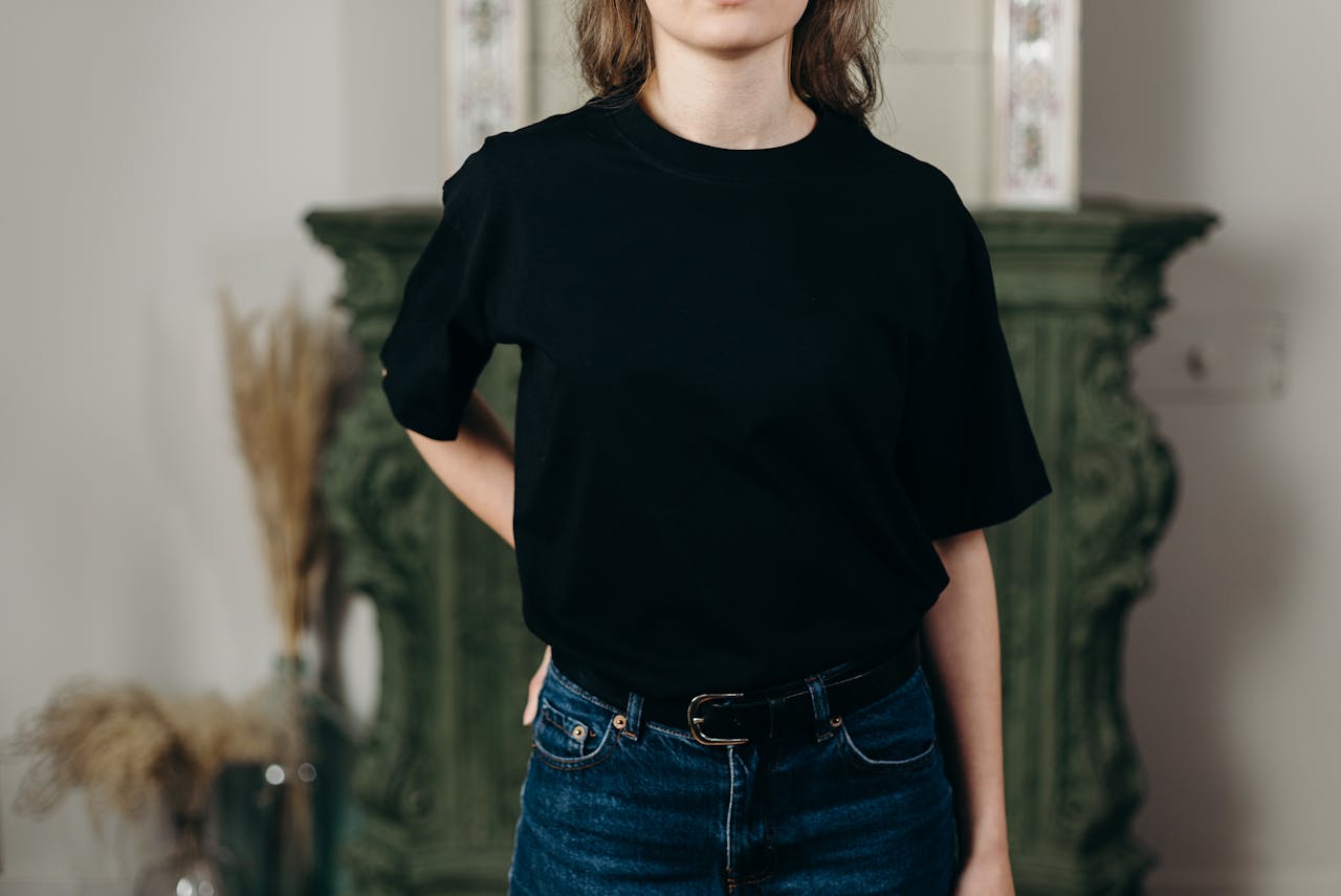 Faceless model in black t-shirt and jeans showcasing minimalist fashion style indoors.